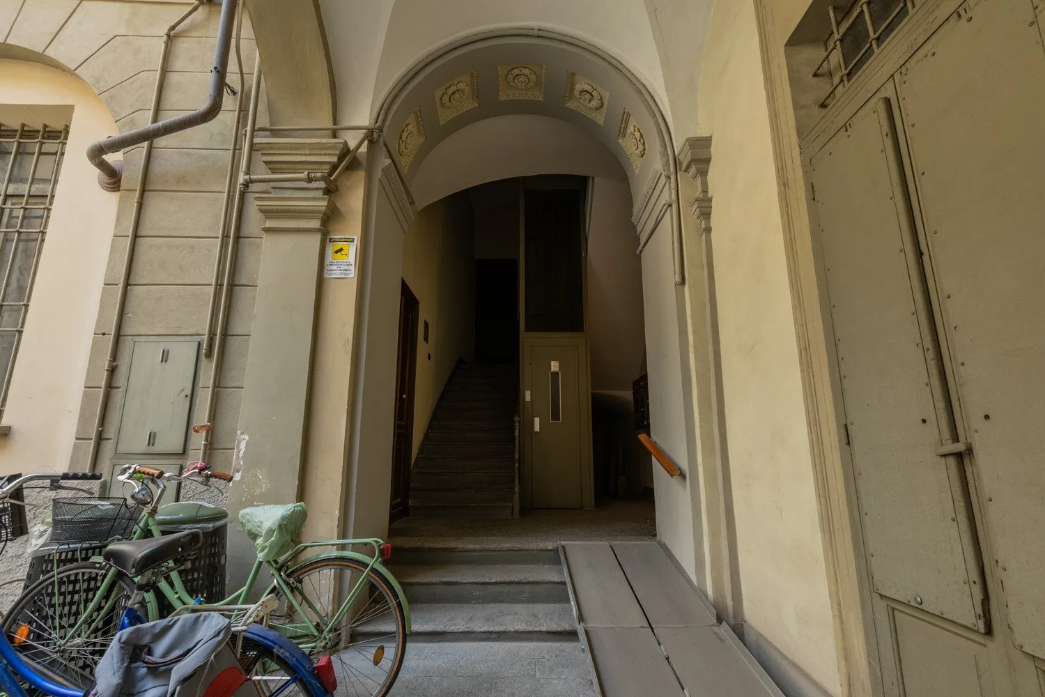 Una entrada de edificio con arco da a una escalera, con bicicletas estacionadas cerca.