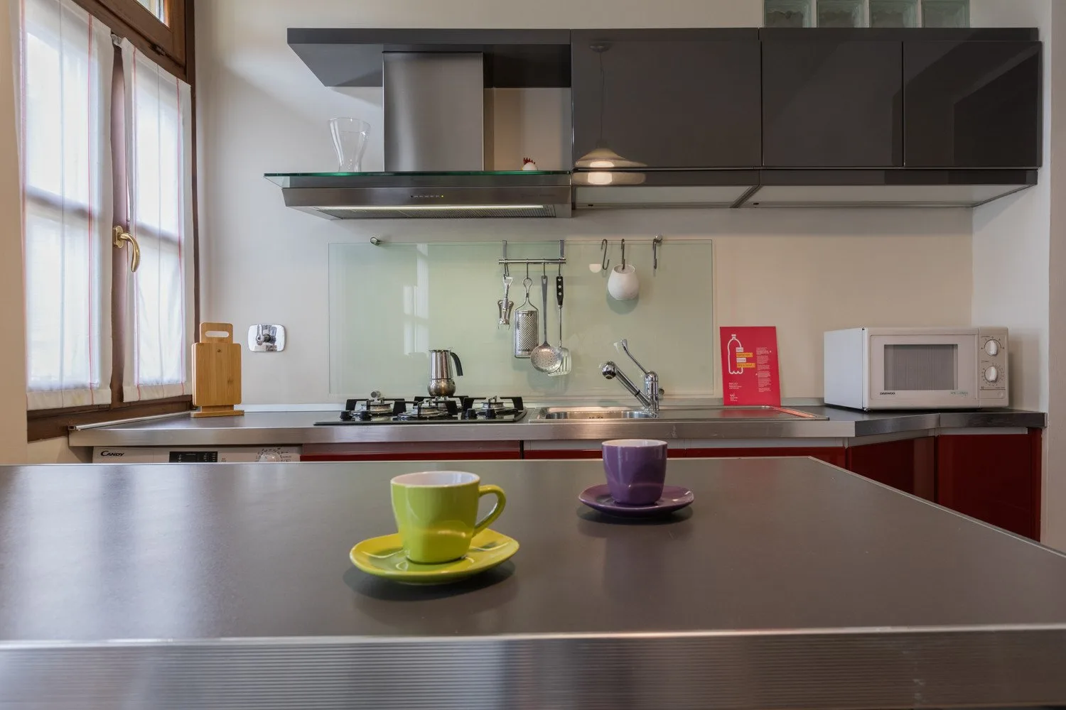 Una cocina con tazas sobre la encimera y electrodomésticos al fondo.