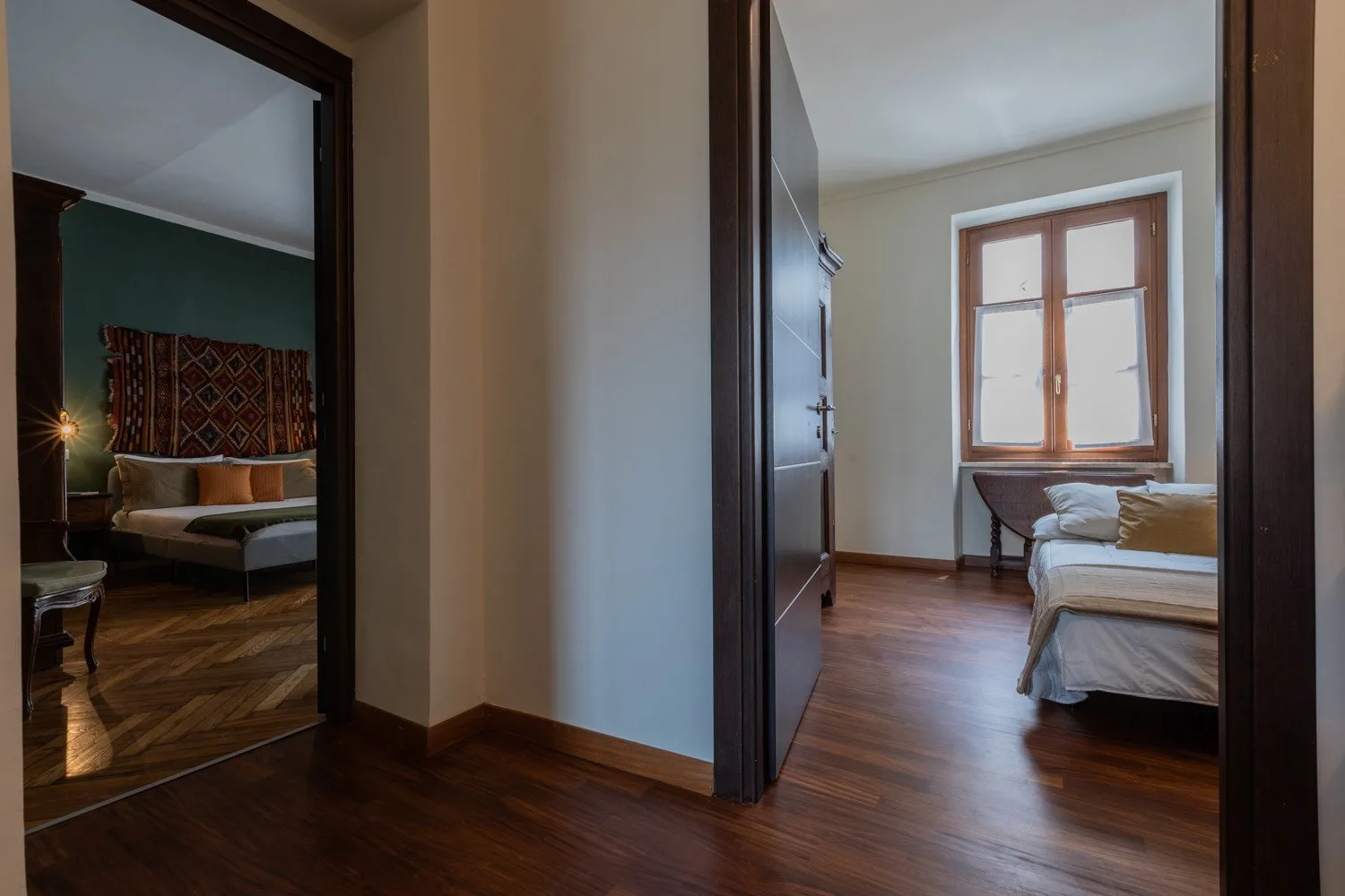 Un pasillo da a dos dormitorios, con suelo de madera y una ventana en la habitación de la derecha.