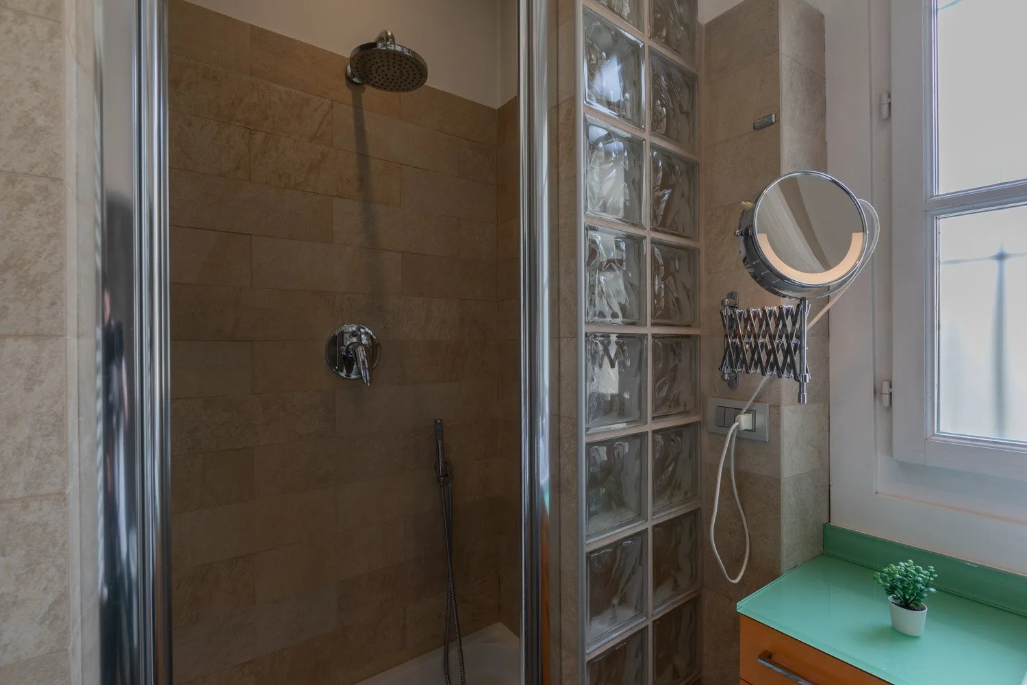Una ducha de baño con azulejos está junto a una pared de bloques de vidrio y una ventana.