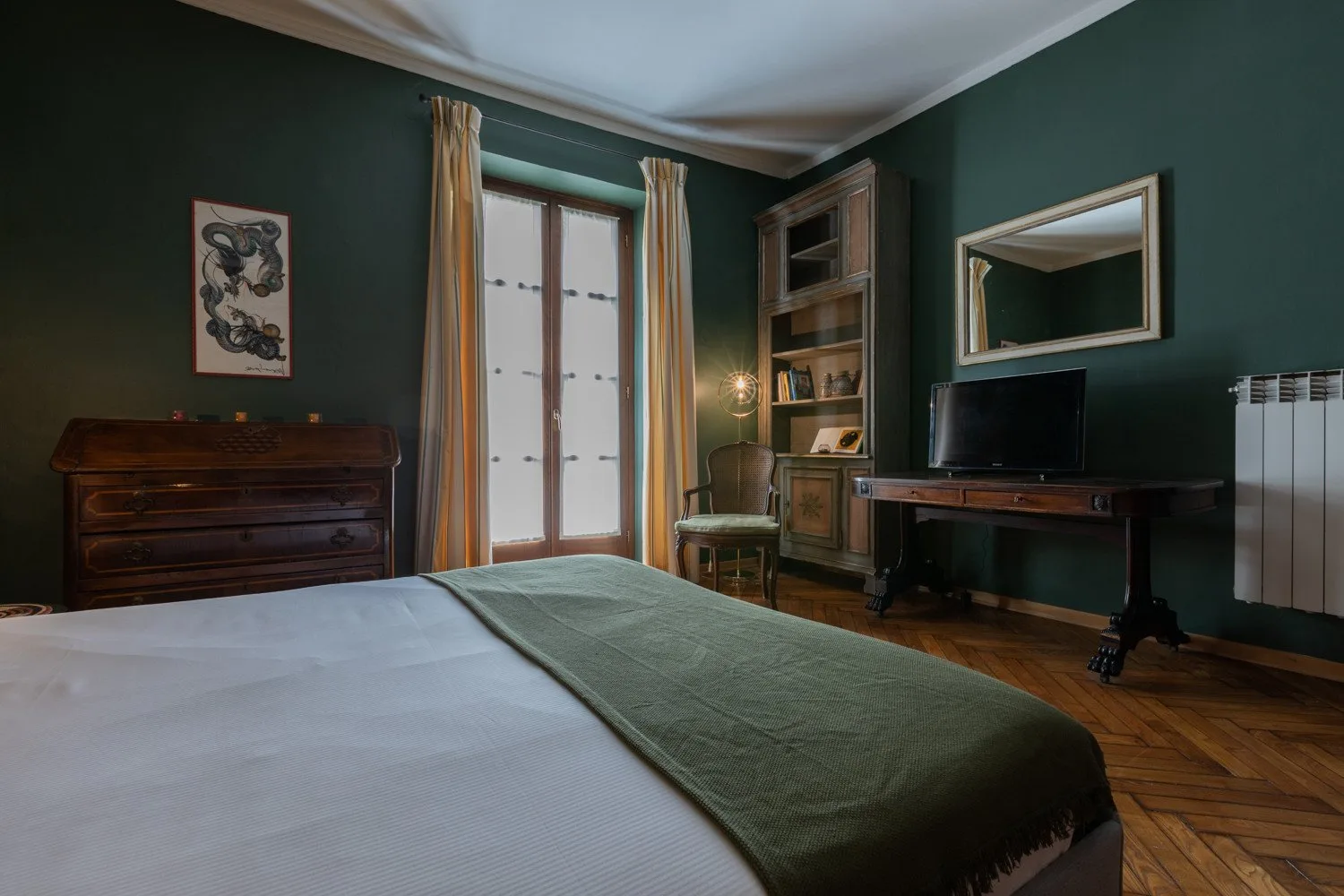 Un dormitorio con una cama, ventanas altas y paredes verde oscuro.