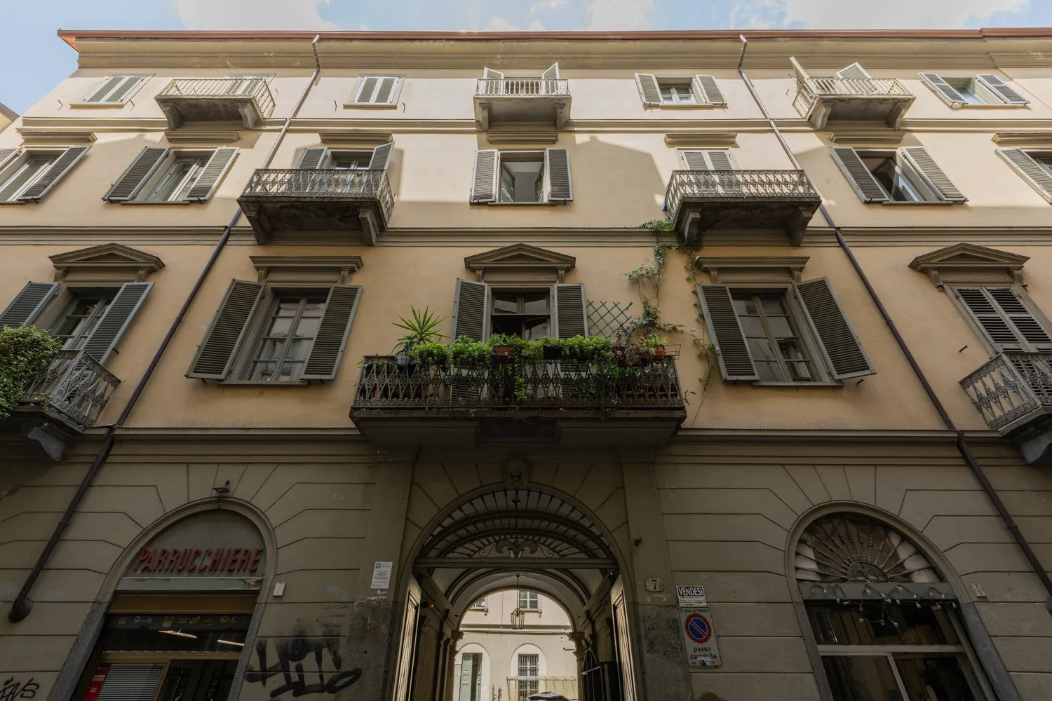Fachada de un edificio de varias plantas con ventanas con persianas, balcones y una entrada arqueada.