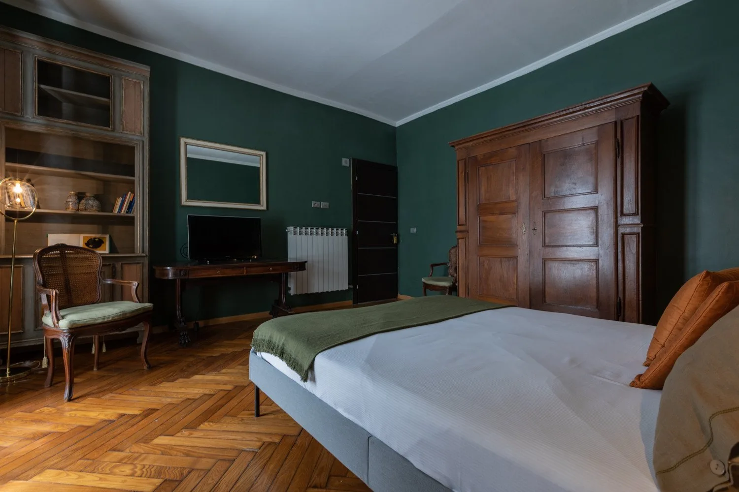 Un dormitorio con una cama bien tendida, paredes verde oscuro y muebles de madera.