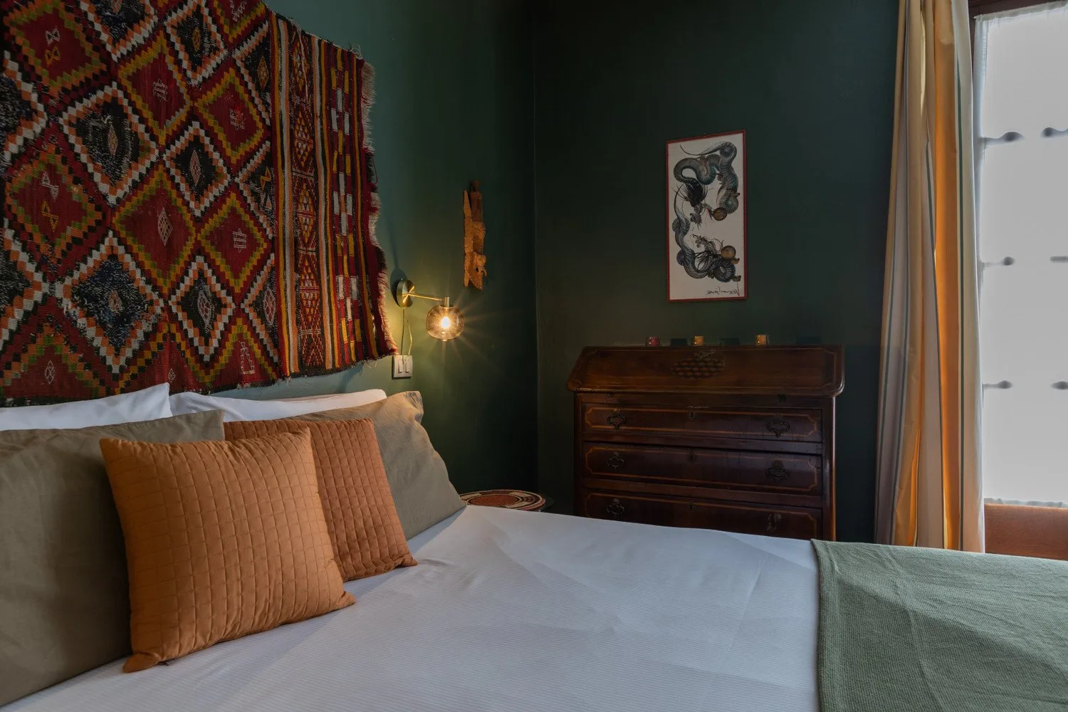 Un dormitorio con una cama, un tapiz estampado y una cómoda de madera oscura.