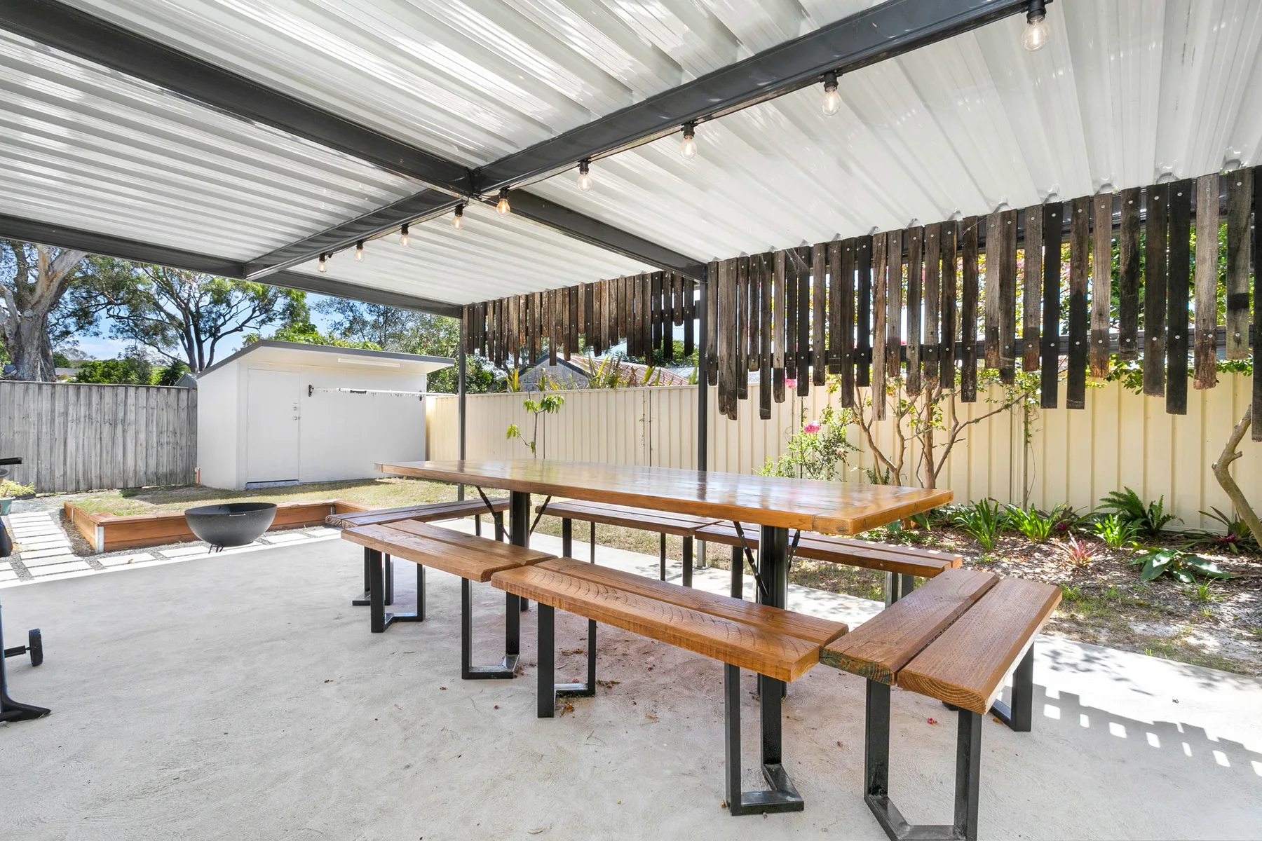Comedor exterior cubierto con mesas largas de madera y bancos.