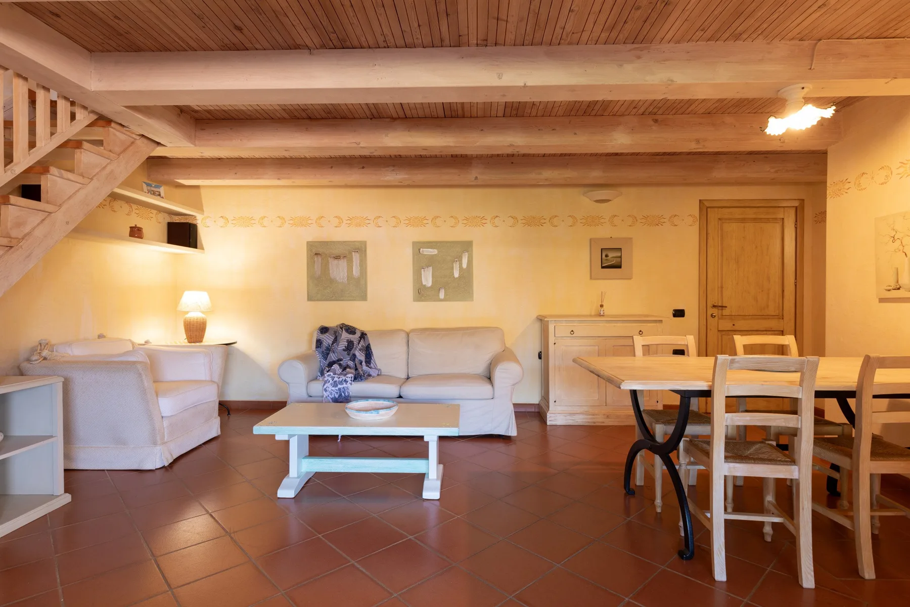 Una sala de estar y comedor con asientos, una mesa de centro y una escalera de madera.