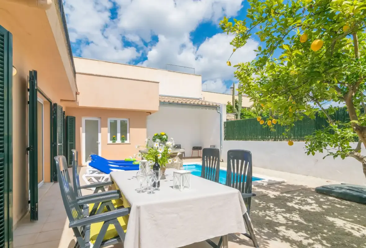 Una zona de comedor al aire libre junto a una piscina y un árbol frondoso.