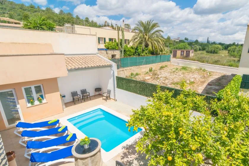 Un patio soleado con piscina y tumbonas azules junto a una casa.