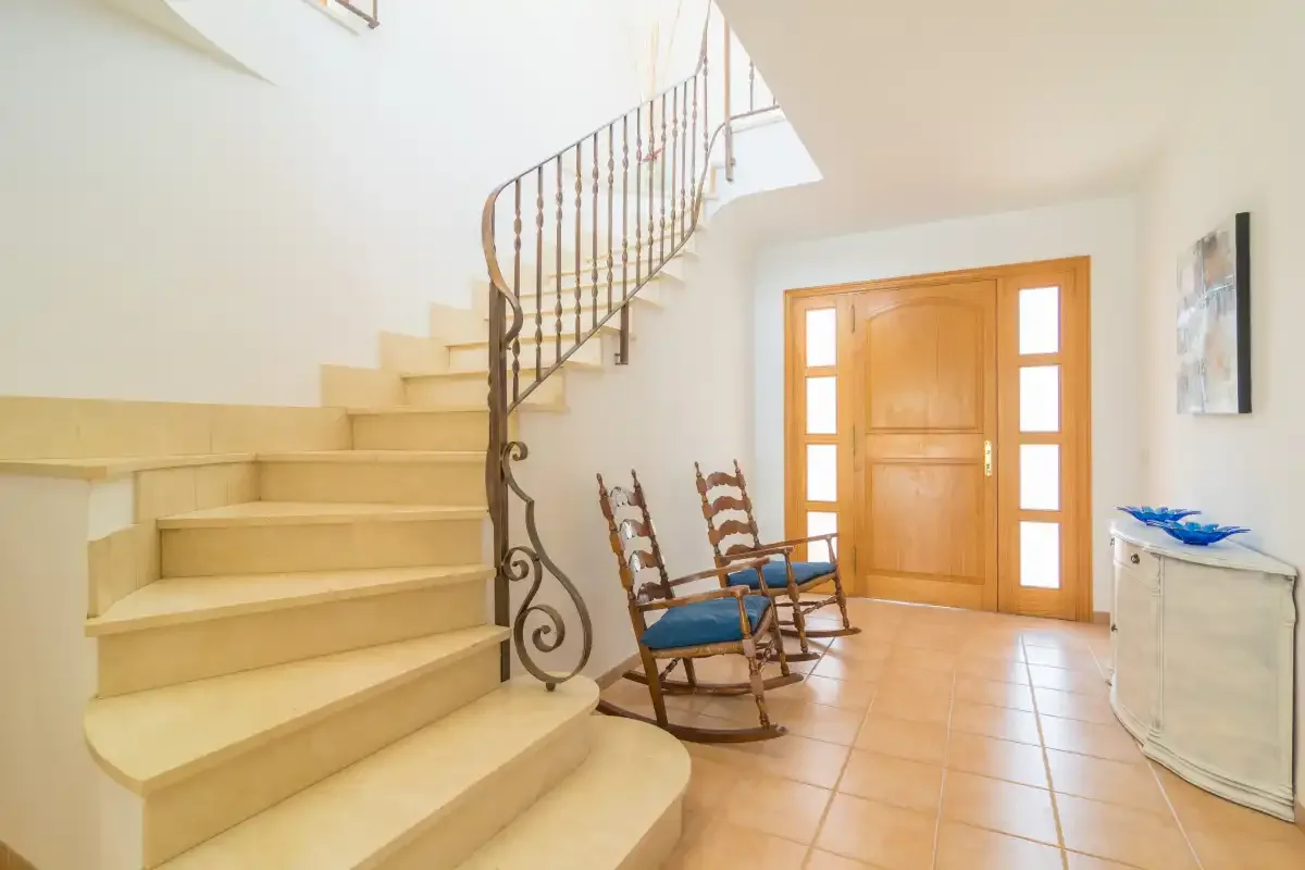 Un recibidor luminoso con una escalera curva, una puerta de madera y suelo de baldosas.