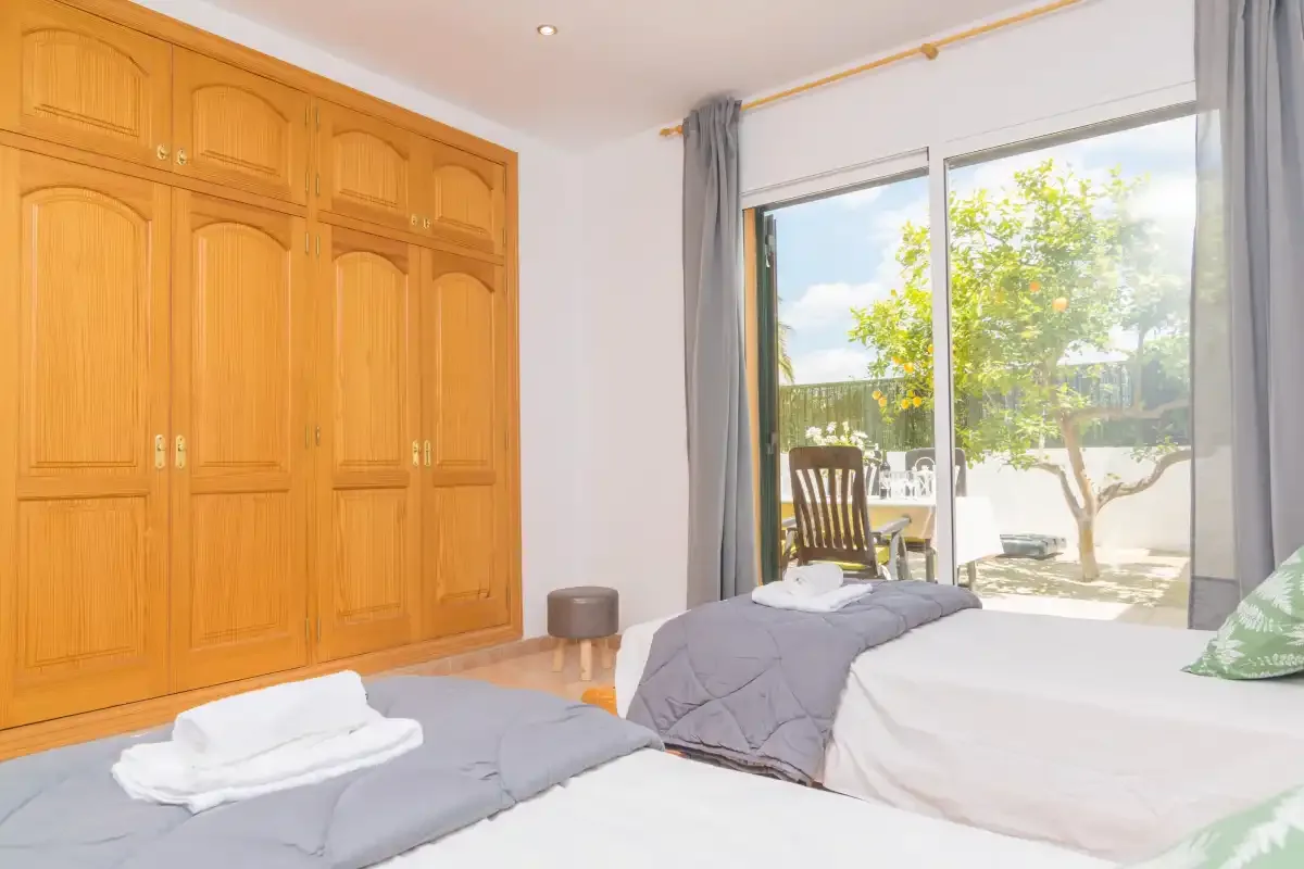 Un dormitorio con camas, armarios de madera y una gran puerta de cristal abierta al jardín.
