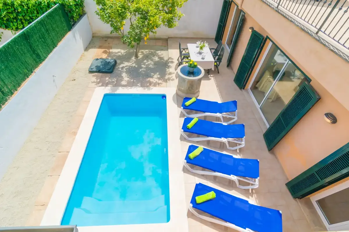 Una piscina en un patio está junto a una fila de tumbonas azules.