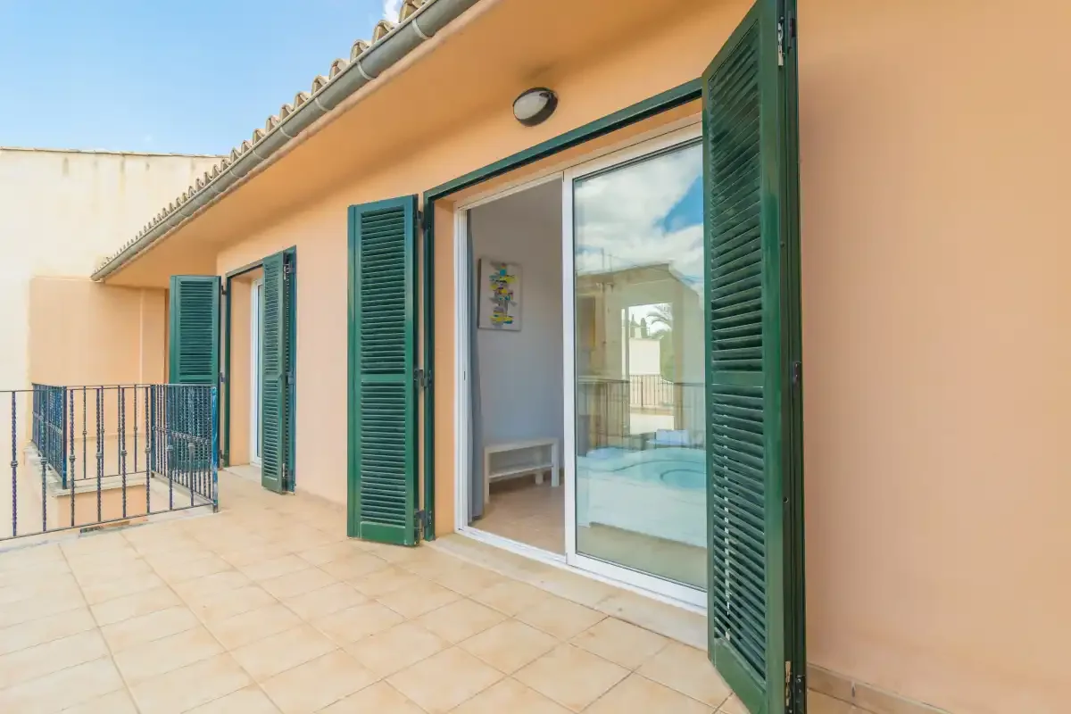 Una terraza de baldosas con contraventanas verdes junto a una puerta corrediza de vidrio.