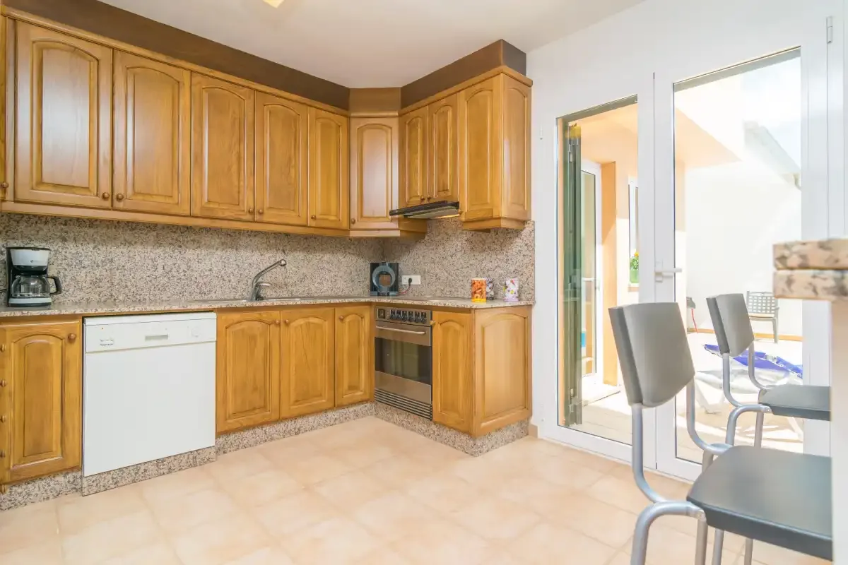 Una cocina con armarios de madera, lavavajillas y una mesa junto a puertas de vidrio.