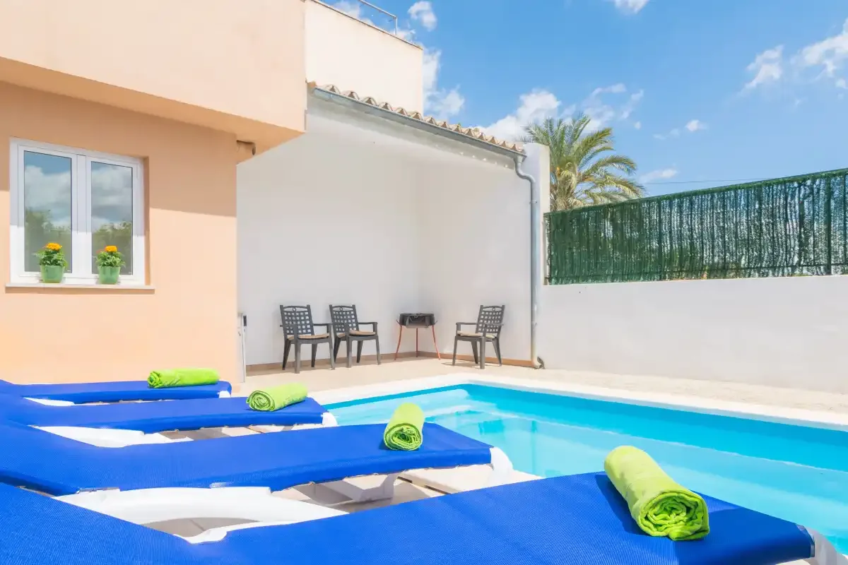 Una piscina al aire libre junto a una terraza soleada con tumbonas azules.