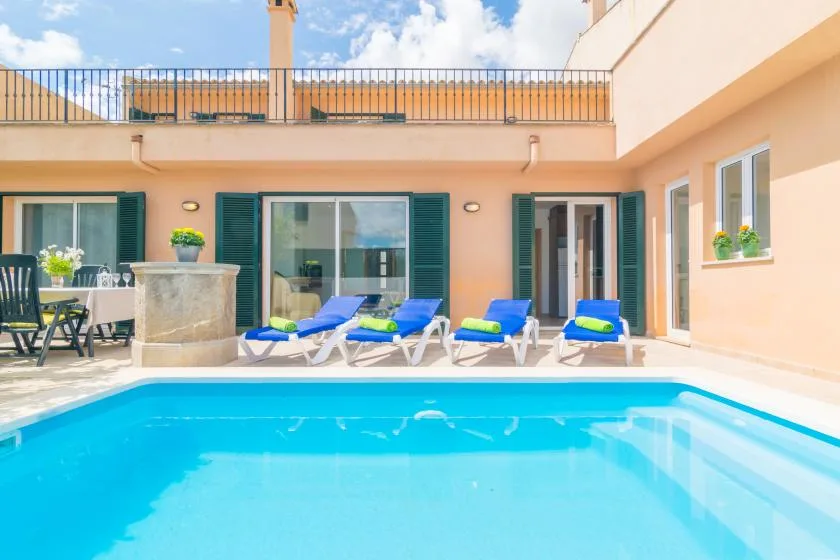 Una piscina está junto a una casa color durazno y tumbonas azules.