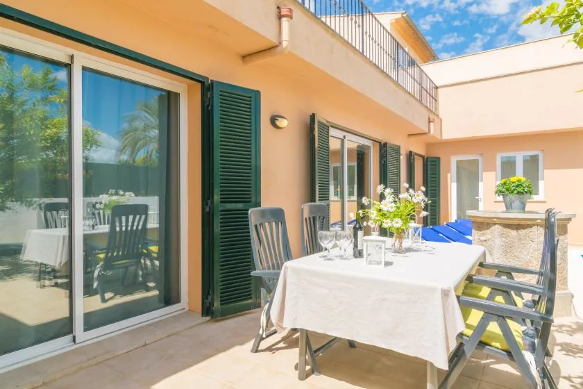 Una terraza soleada con una mesa y asientos junto a grandes puertas de vidrio.