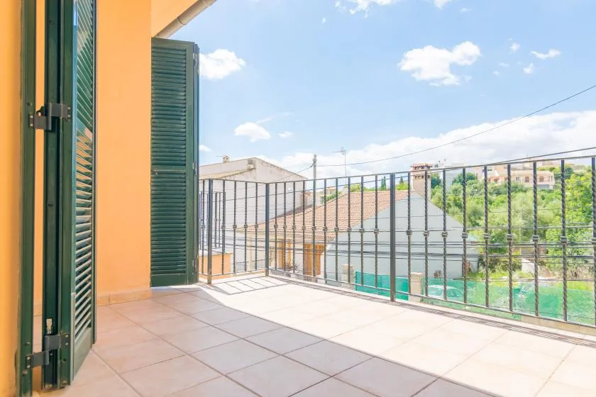 Un balcón de baldosas con contraventanas verde oscuro da a tejados y árboles cercanos.