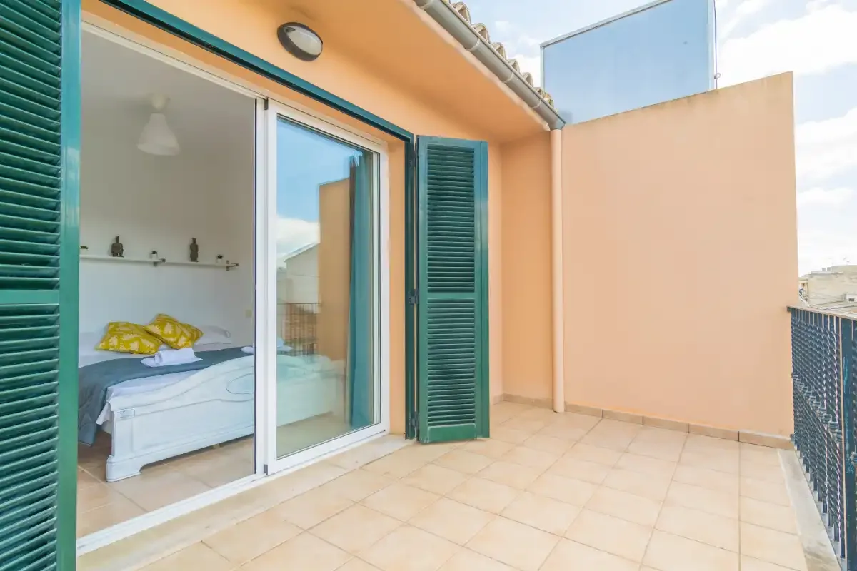 Una terraza embaldosada da a un dormitorio con puertas corredizas de vidrio y contraventanas verdes.