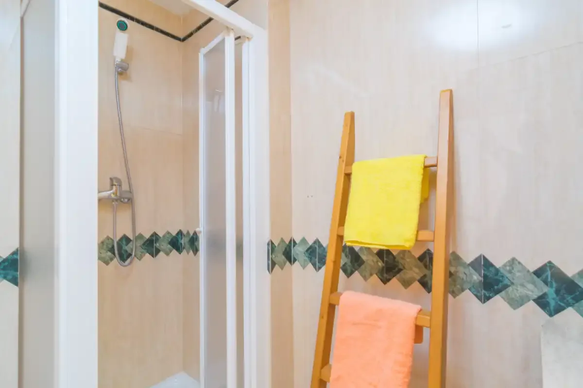 Un baño alicatado con ducha y una escalera de madera para toallas.