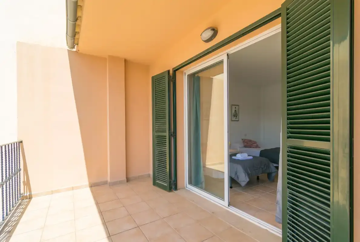 Un balcón embaldosado con contraventanas verdes da a un dormitorio.