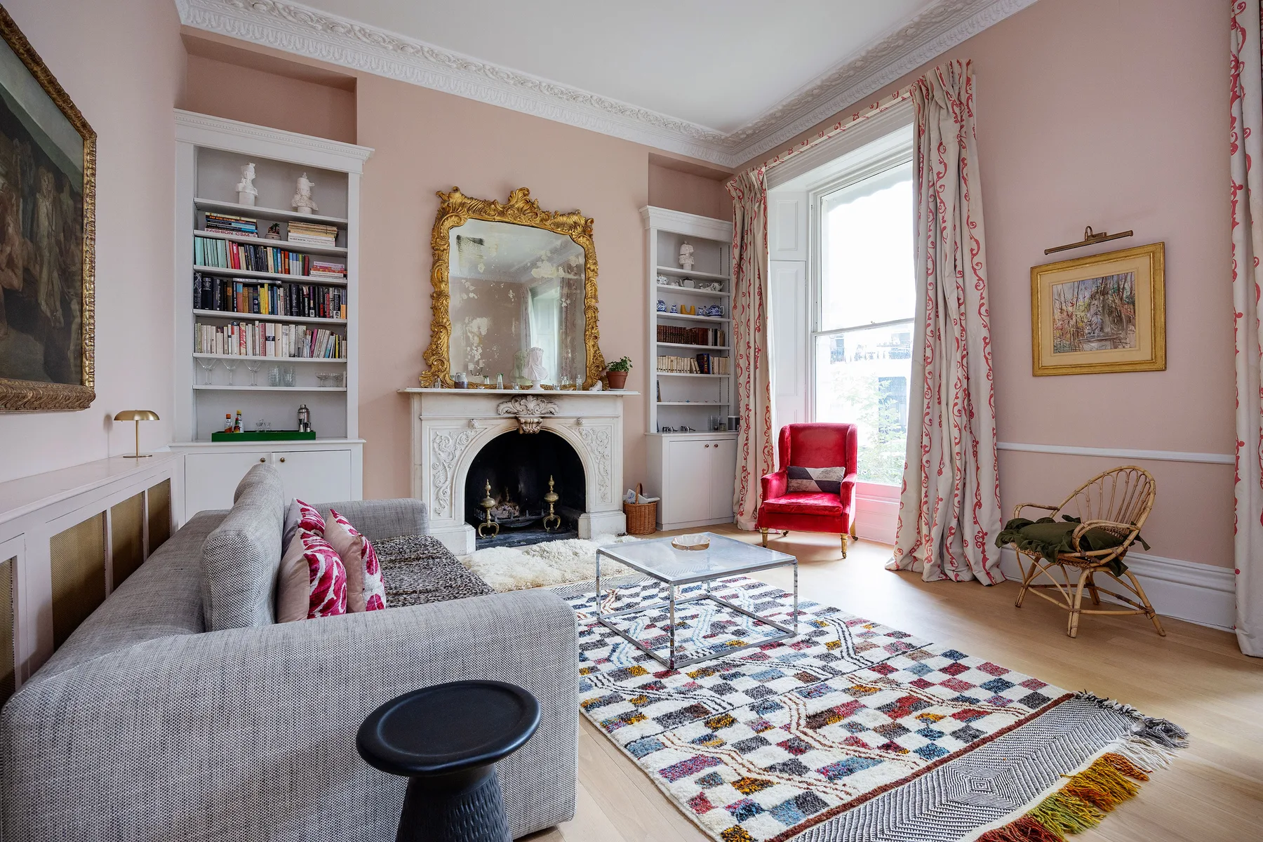 Una sala de estar rosa con chimenea, estanterías y una alfombra estampada.
