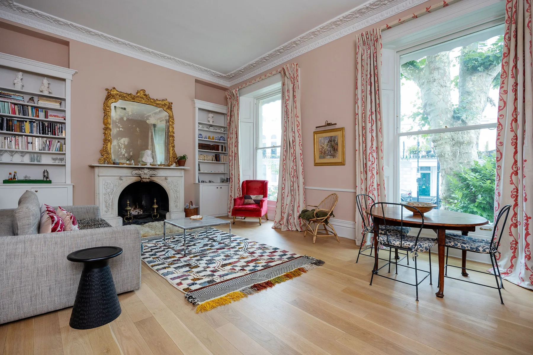 A bright living room with a fireplace, seating, and a dining table by large windows.