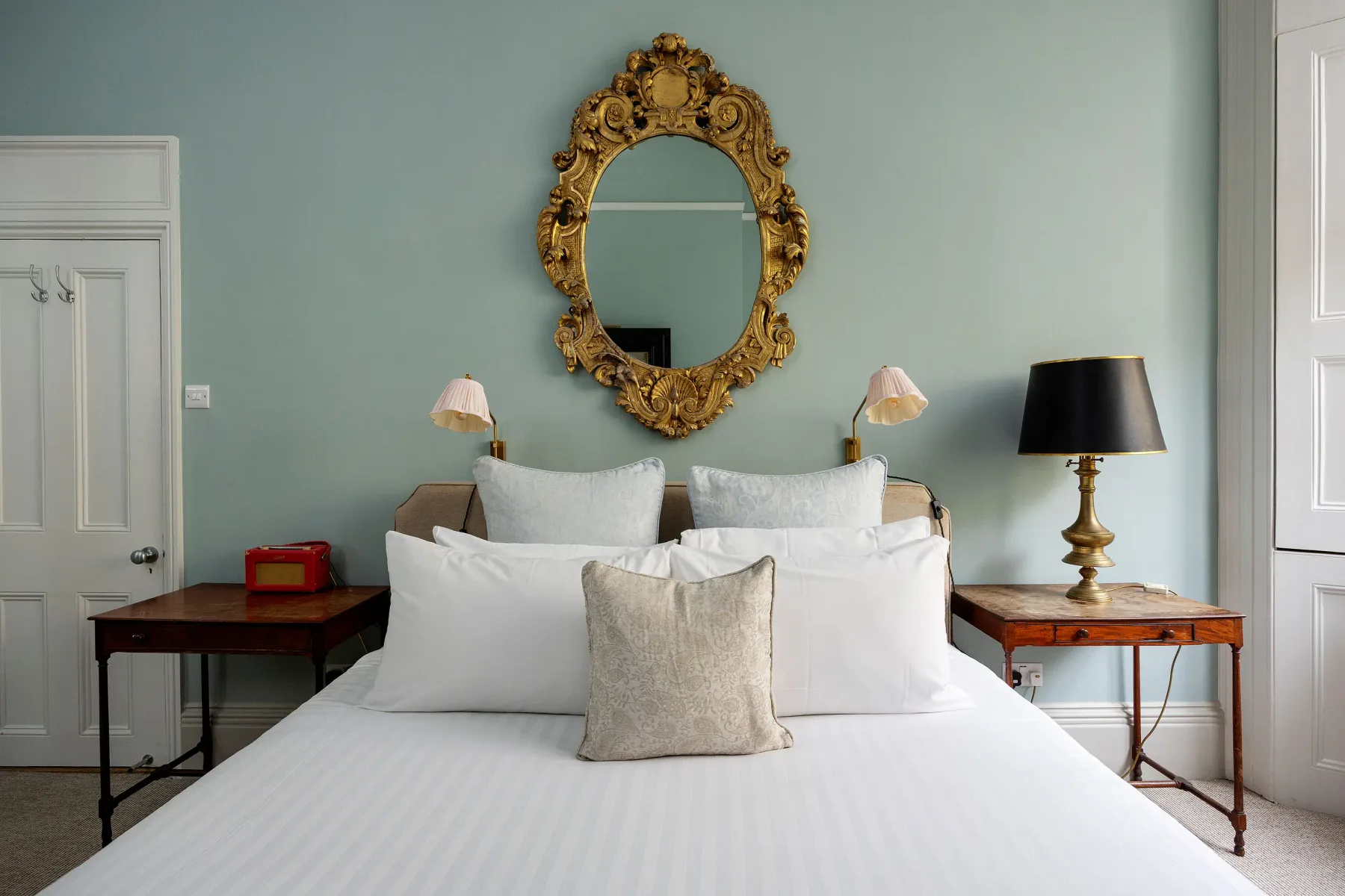 Un dormitorio con una cama bien hecha y un espejo ornamentado encima.