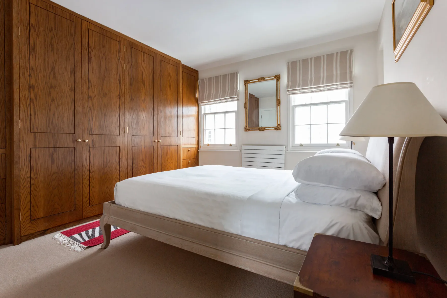 A bright bedroom with a bed, tall wooden cabinets, and two windows.