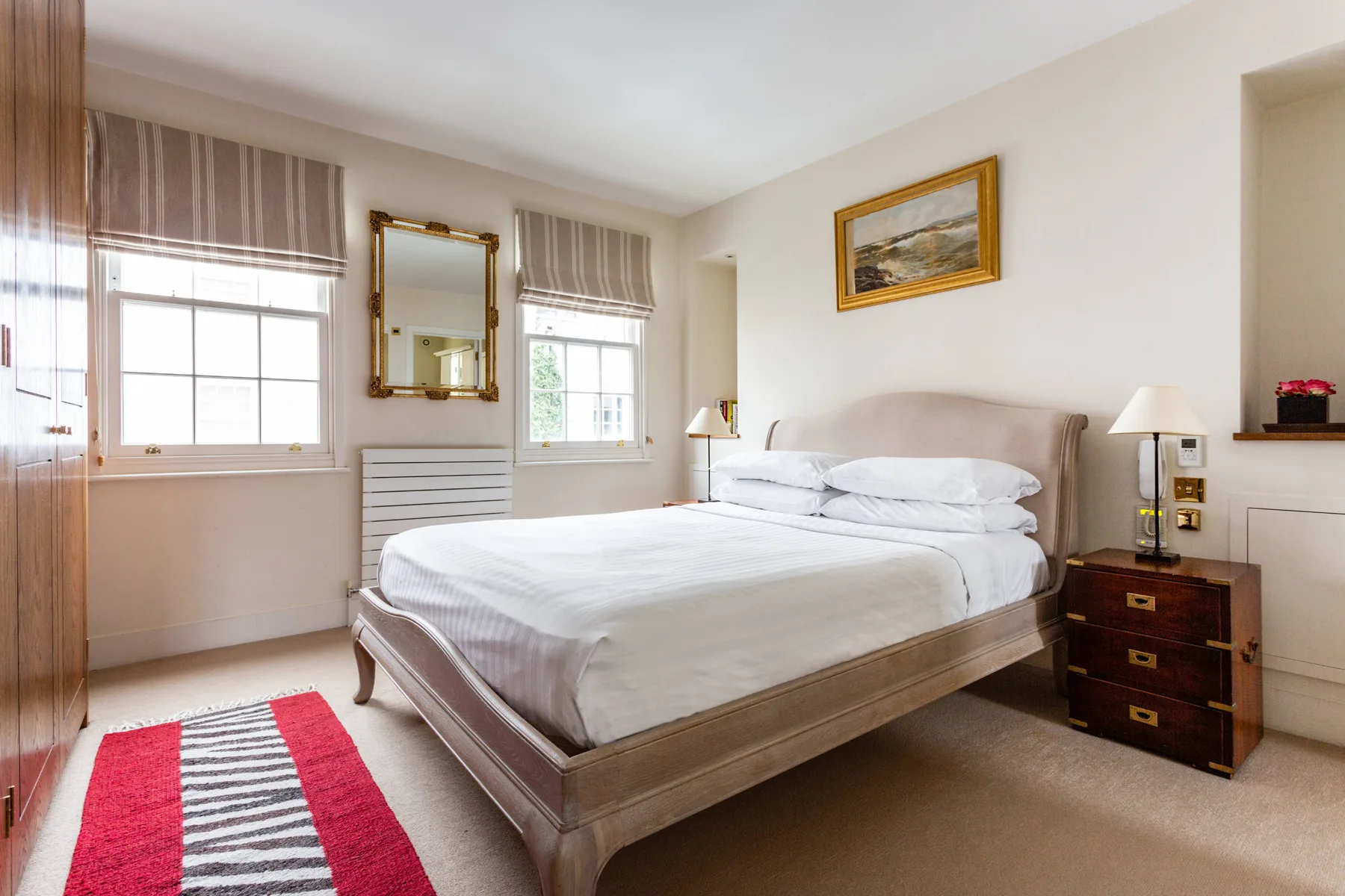 A bright bedroom with a neatly made bed, large windows, and a bedside table.