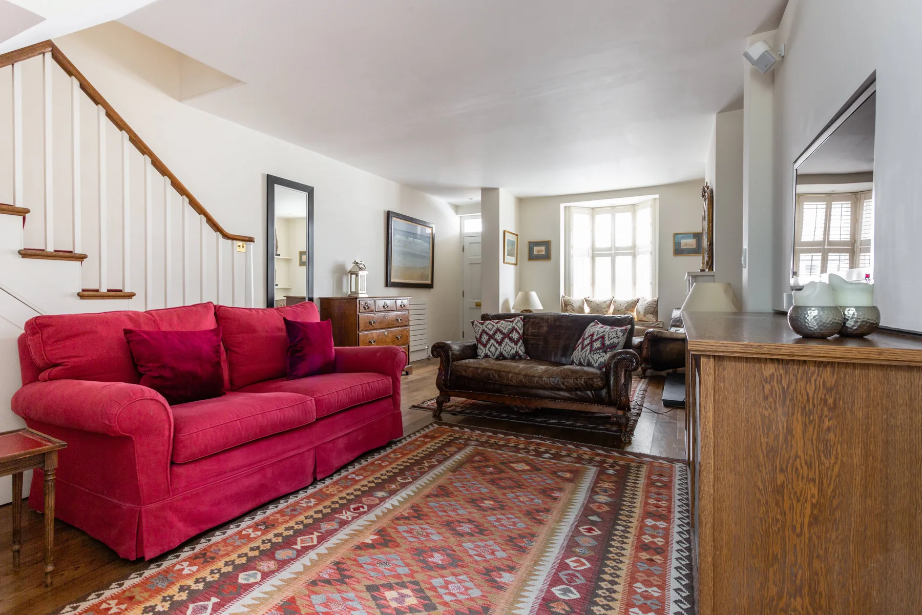 A living room with red seating, a patterned rug, and a wooden staircase.