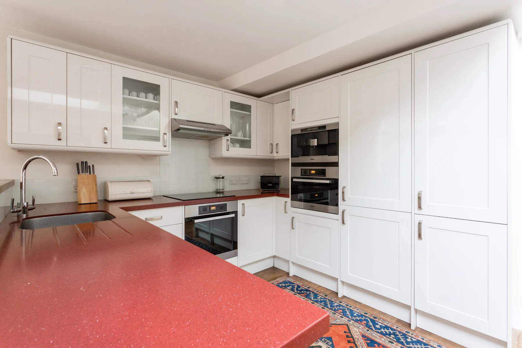 A bright kitchen with white cabinets, built-in appliances, and red countertops.