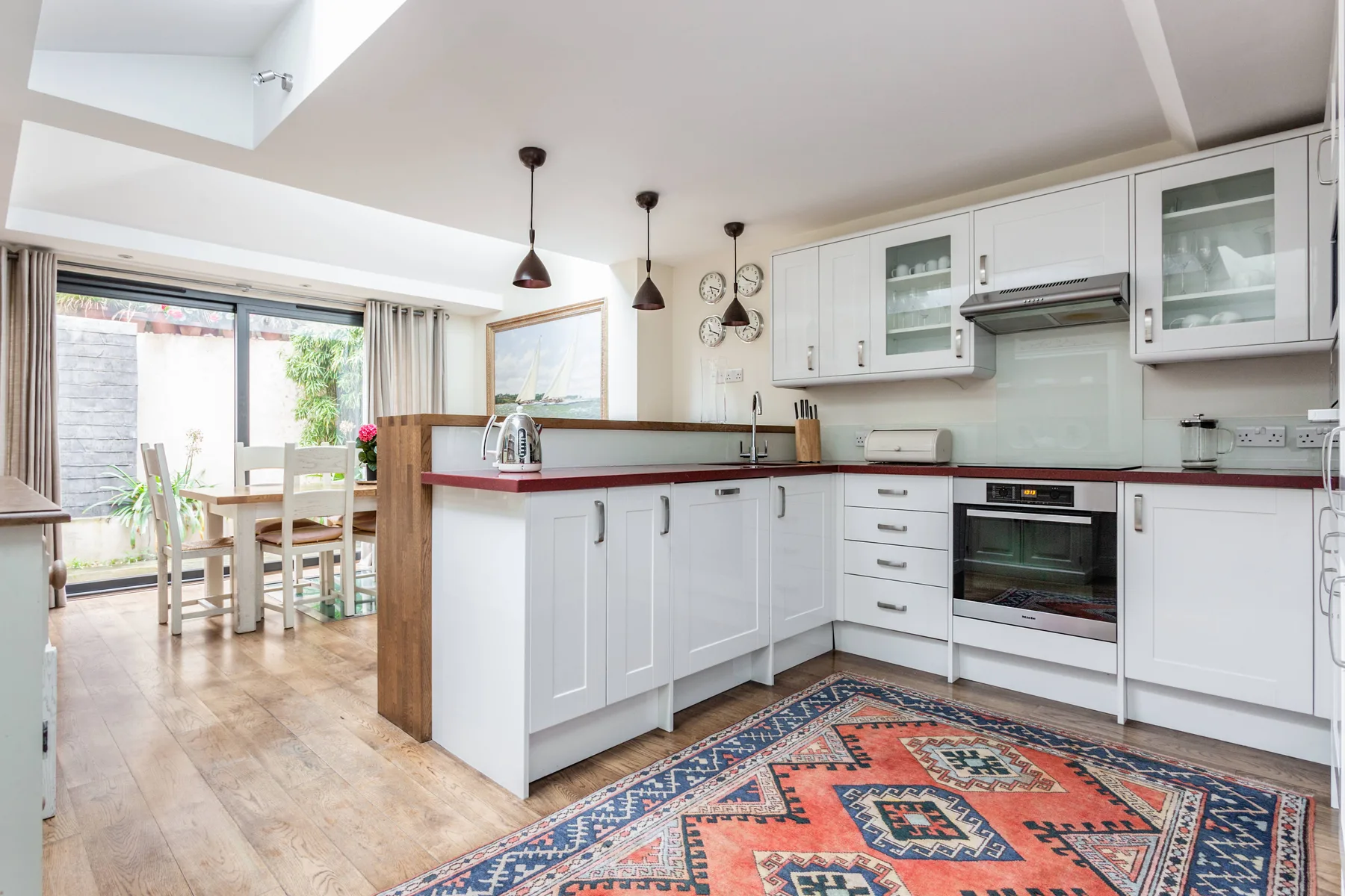 A bright kitchen with white cabinets, a breakfast bar, and a patterned rug.