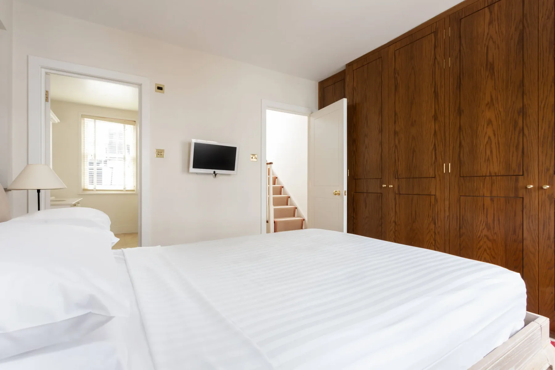 A bedroom with a neatly made bed and a large wooden wardrobe.