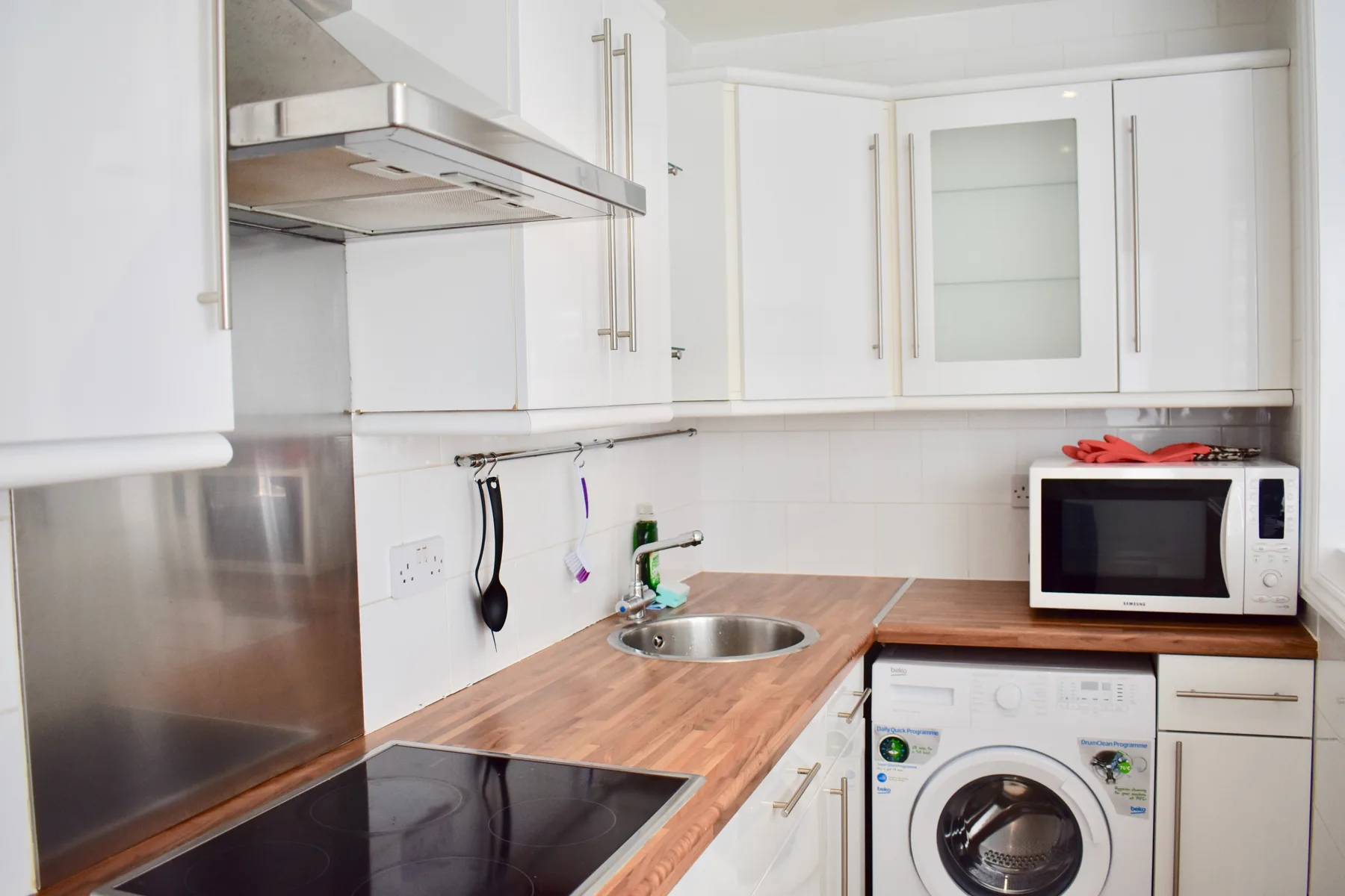 Una cocina compacta con fregadero, placa de cocina, microondas y lavadora.