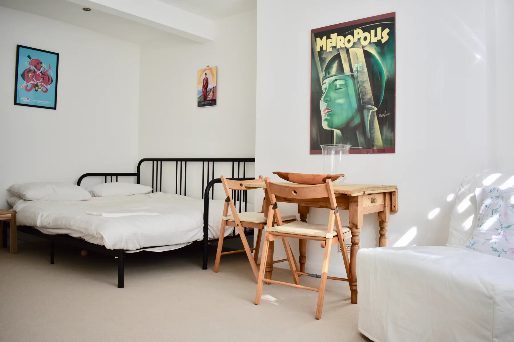 Un dormitorio luminoso con una cama, una mesa de madera y pósteres enmarcados.