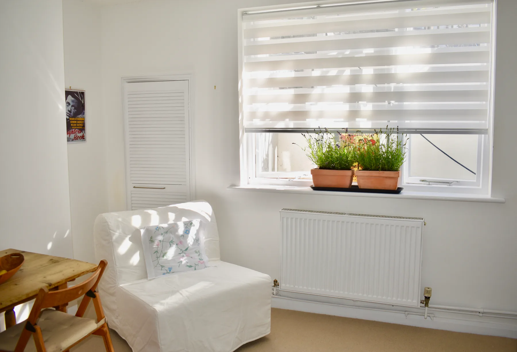 Una zona de estar luminosa con un asiento cubierto, una ventana y plantas en macetas.