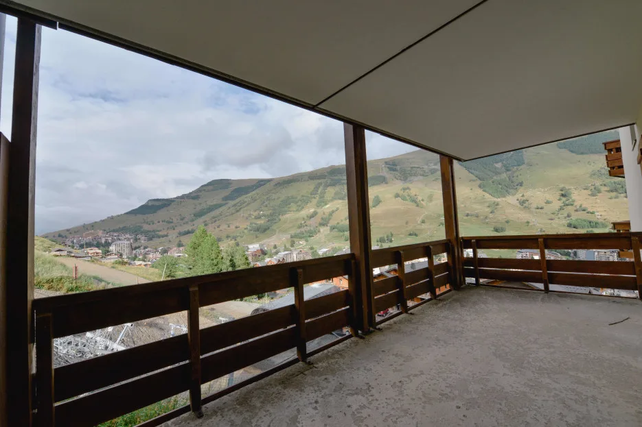 A covered balcony overlooks a hillside town and green mountains.