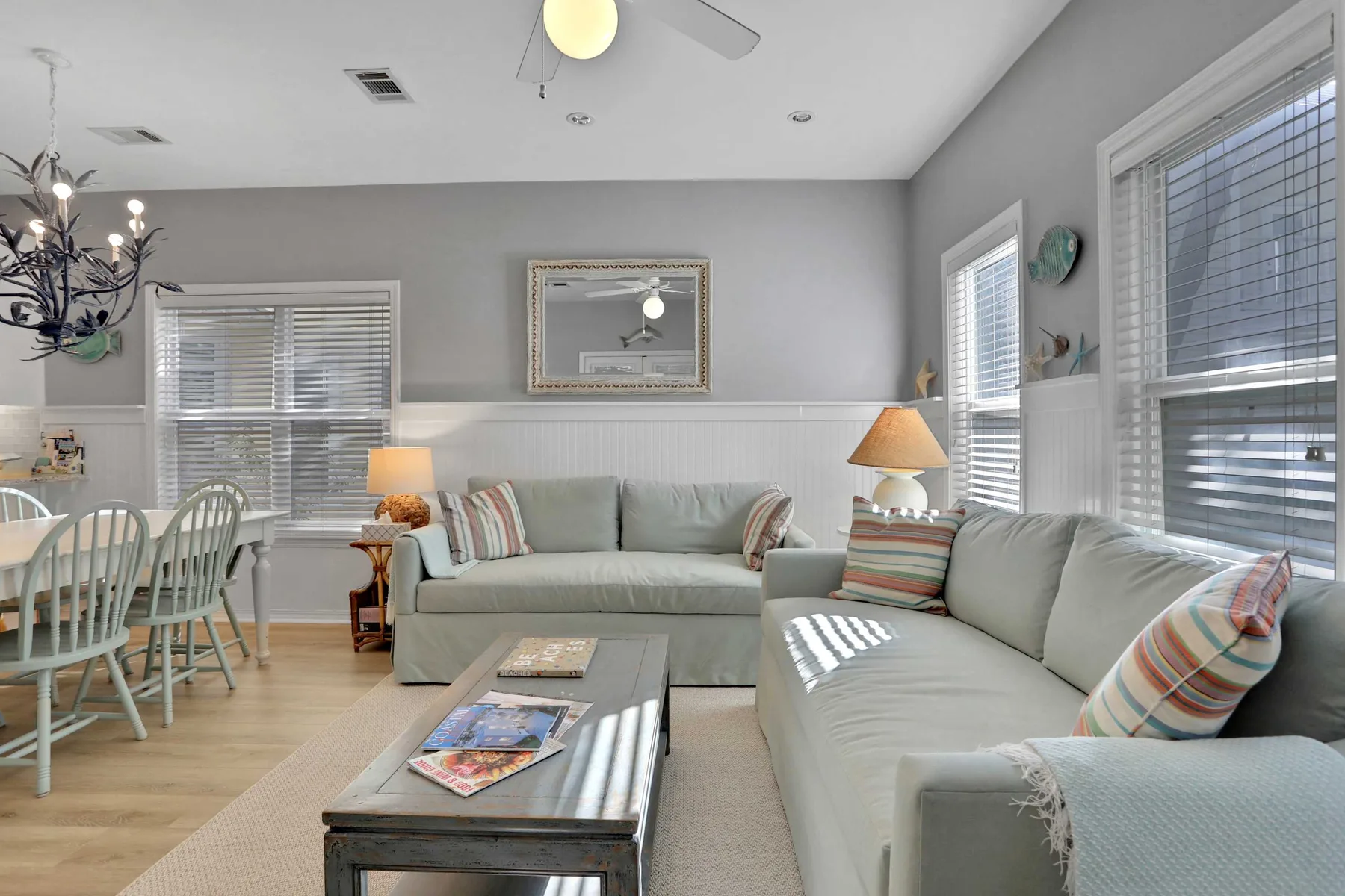 Sala de estar con asientos claros, una mesa de centro y un comedor junto a las ventanas.