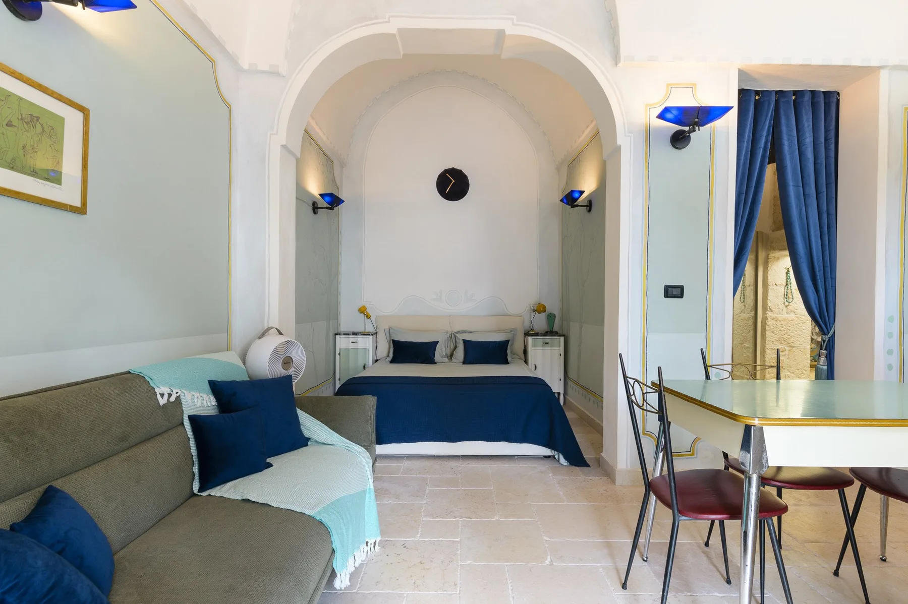 Dormitorio con cama, zona de estar y mesa de comedor bajo un arco.