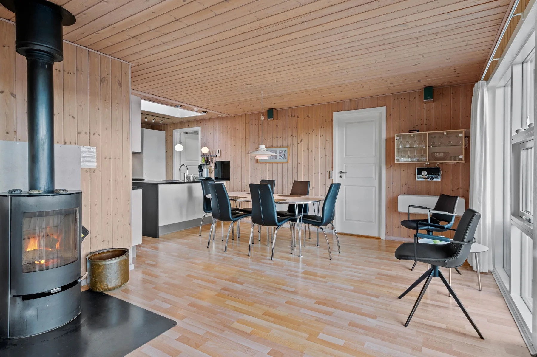 Un comedor y sala con paneles de madera, una mesa, asientos y una estufa encendida.