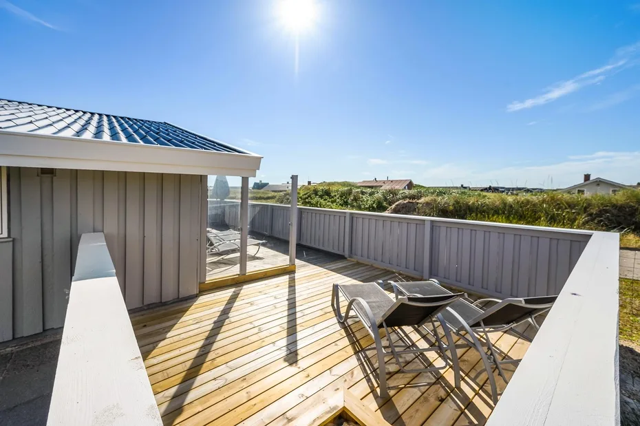 Una terraza exterior soleada con asientos da a una cerca baja y al cielo abierto.
