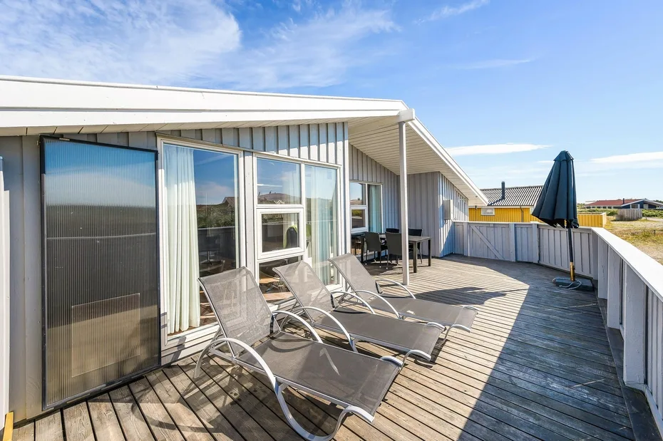 Una terraza exterior soleada junto a un edificio, con asientos reclinables y una sombrilla cerrada.