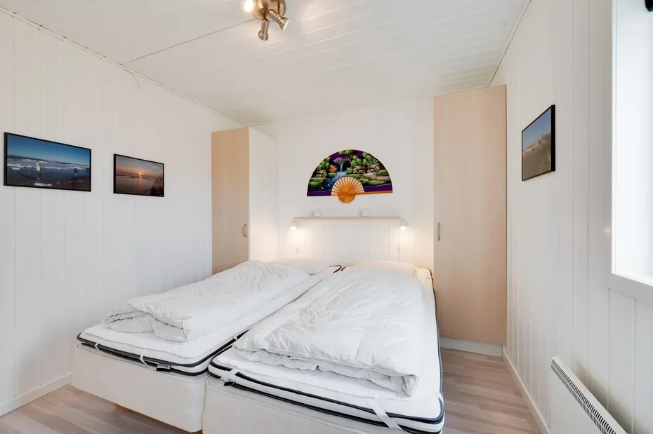 Un dormitorio luminoso con dos camas bajo un abanico decorativo de pared.