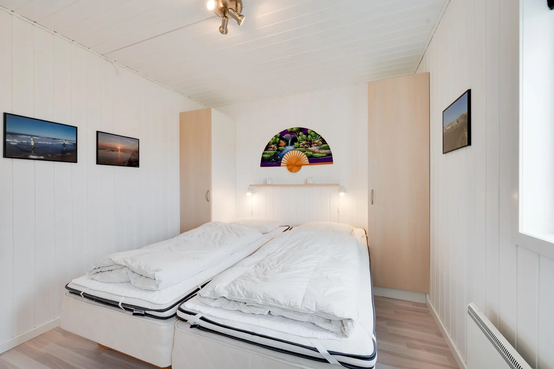 Un dormitorio luminoso con dos camas, ropa de cama blanca y cuadros en las paredes.