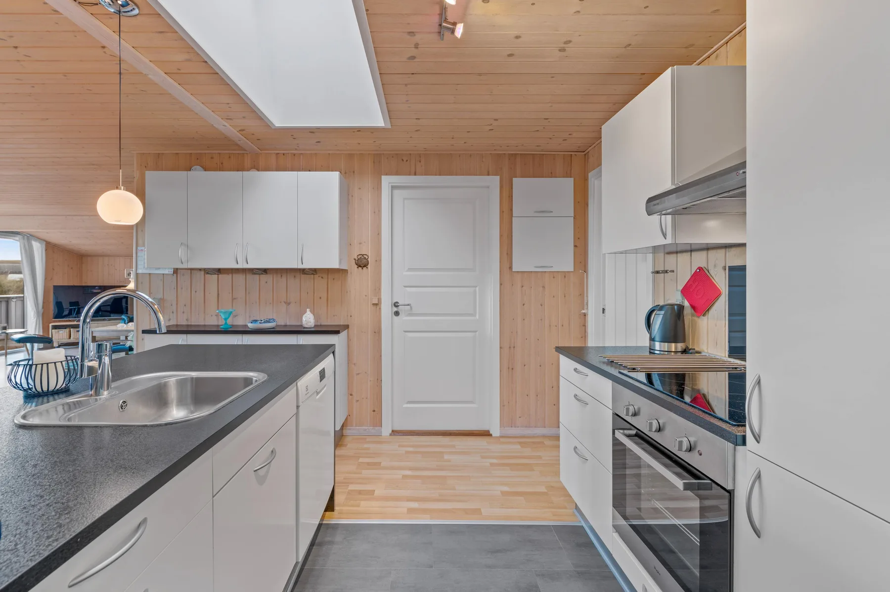 Una cocina luminosa con encimeras y electrodomésticos a ambos lados de un pasillo central.