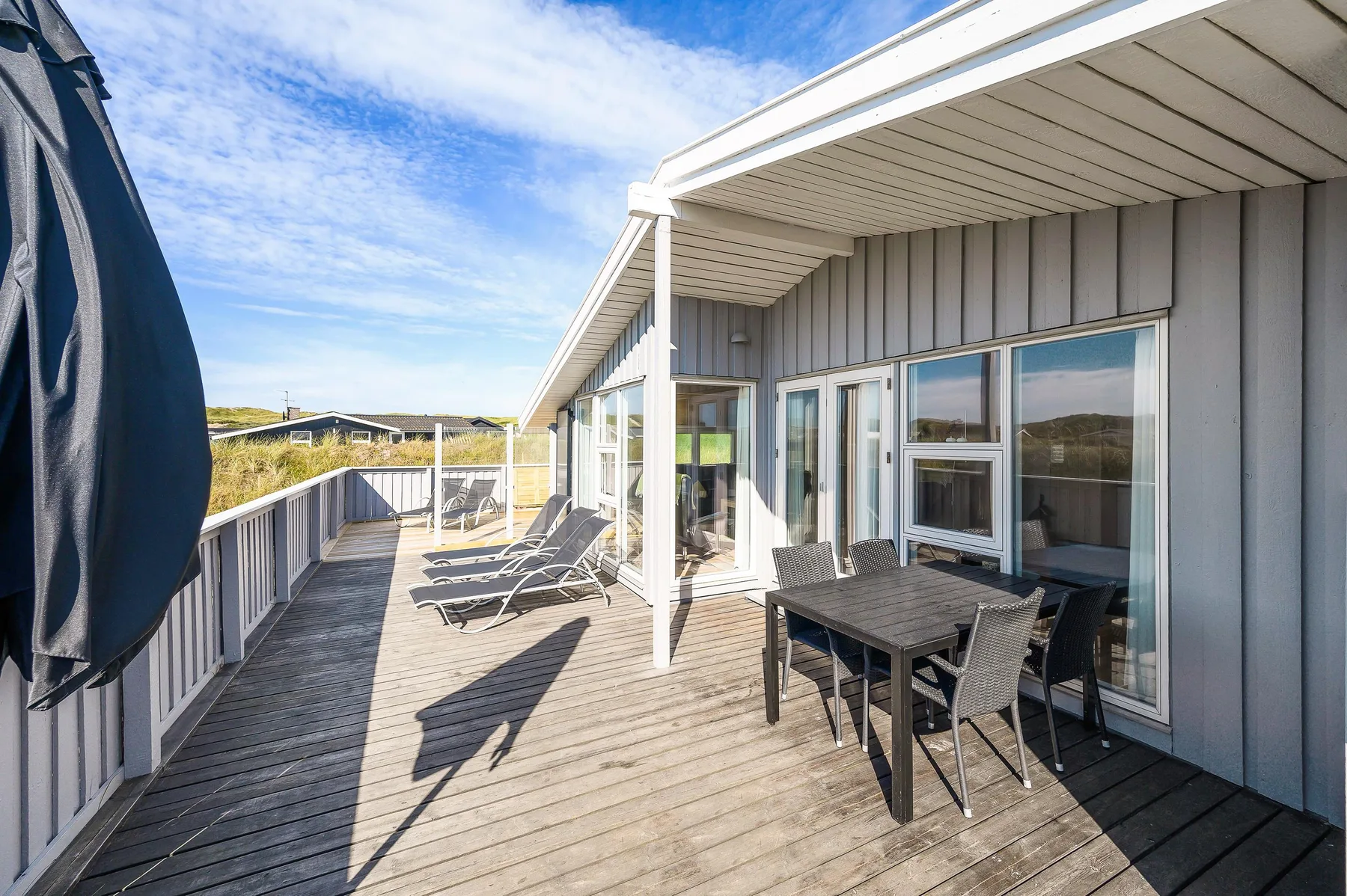 Una terraza de madera soleada con asientos al aire libre junto a una casa.