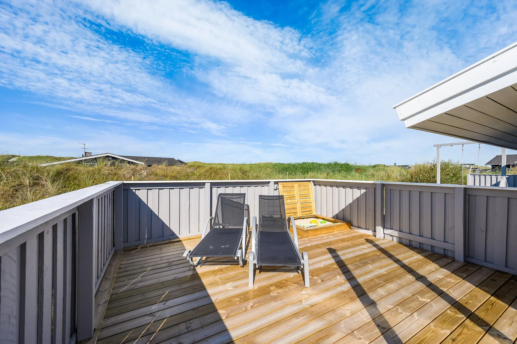 Una terraza exterior soleada con asientos reclinables y una barandilla de madera.