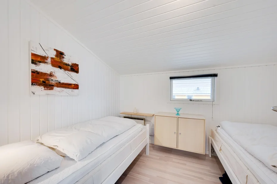 Un dormitorio luminoso con dos camas, un mueble bajo y arte abstracto en la pared.