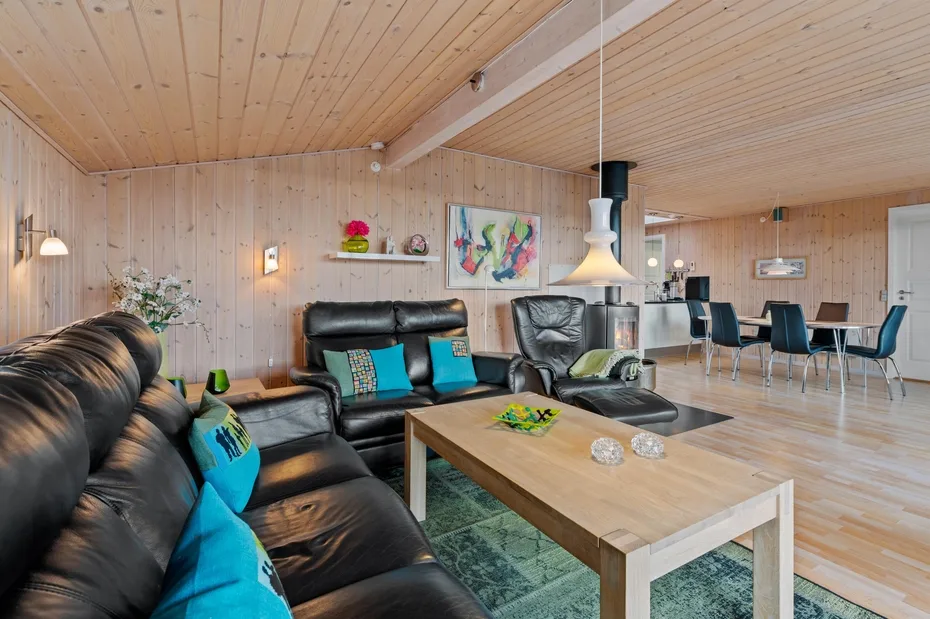 Sala y comedor revestidos de madera, con asientos oscuros y una mesa alargada.