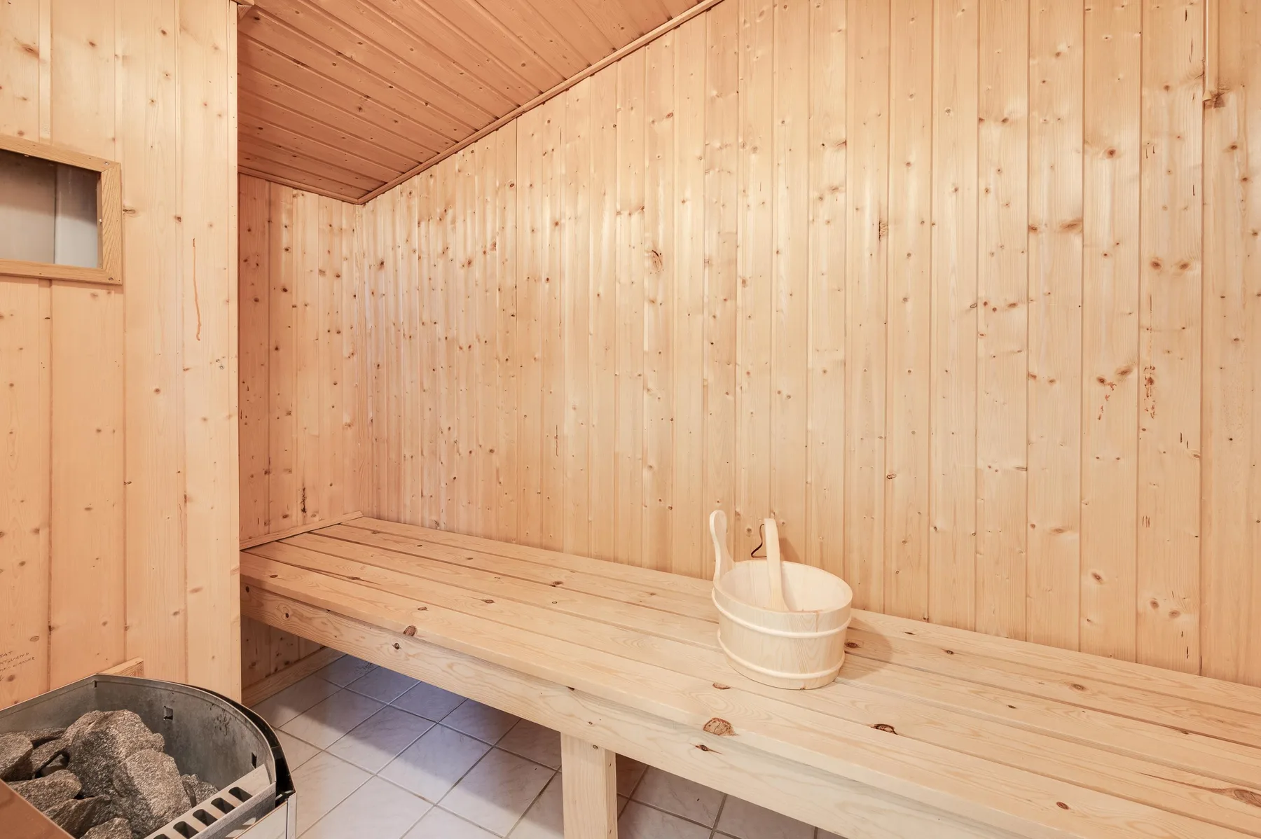 Una sauna revestida de madera con un banco largo y un cubo.